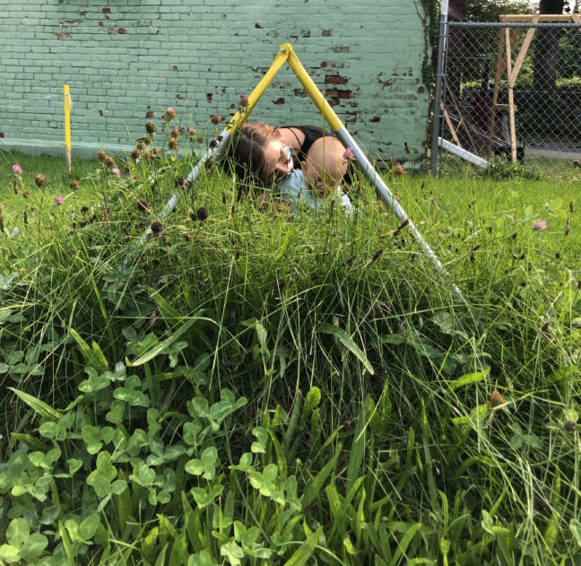 demonstrating one aspect of the audio tour: woman sitting behind pyramid sculpture in the grass